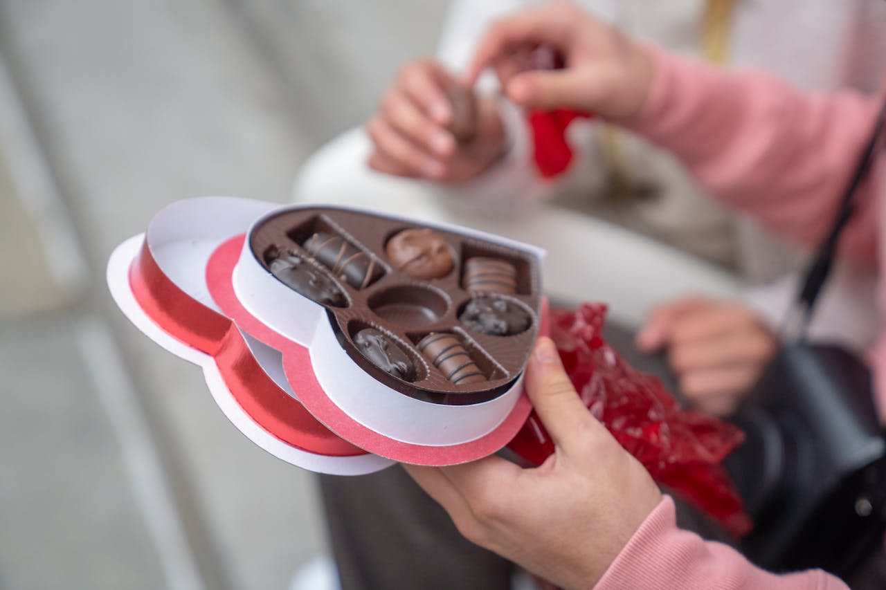 Heart-shaped chocolate box being shared in an affectionate gesture outdoors.